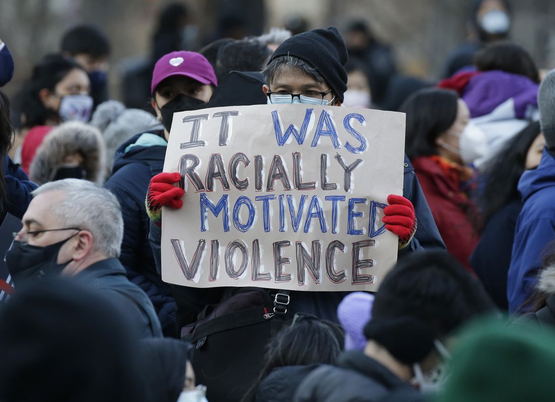 A person holds a sign that says "It was racially motivated violence"